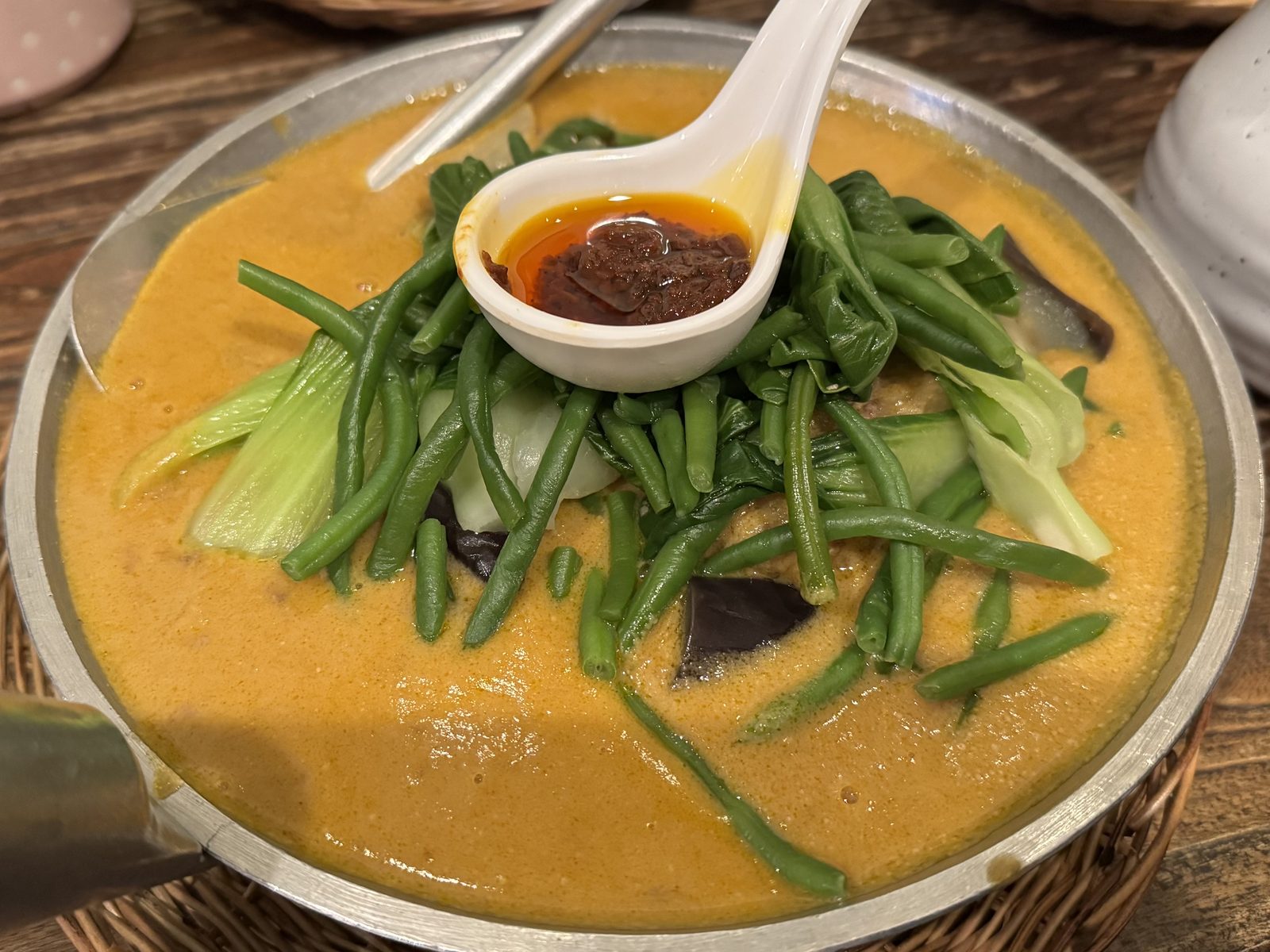 A bowl of Kare-Kare, oxtail and vegetables in a thick peanut sauce, with a side of shrimp paste
